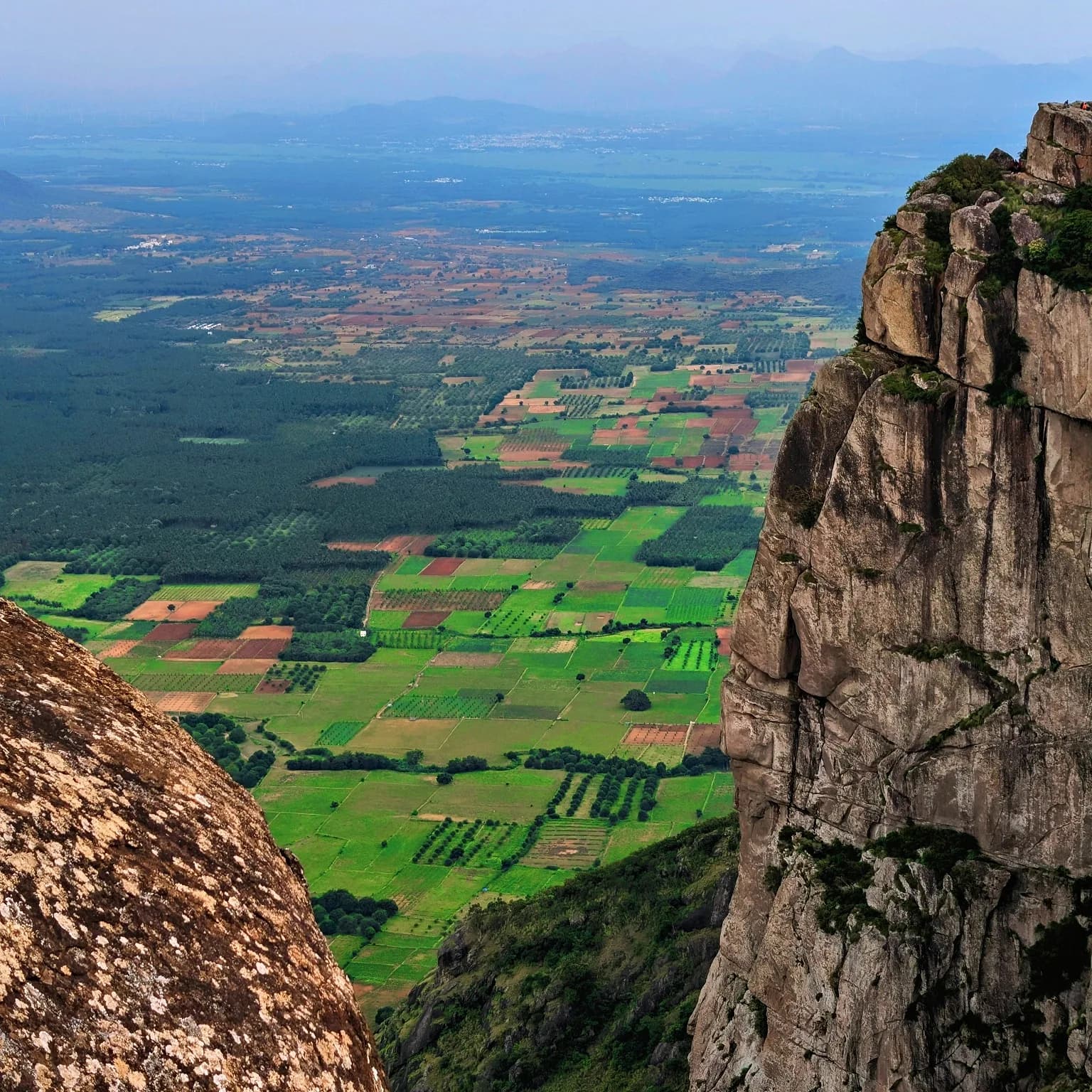 A rocky cliff overlooking a patchwork of green farmland