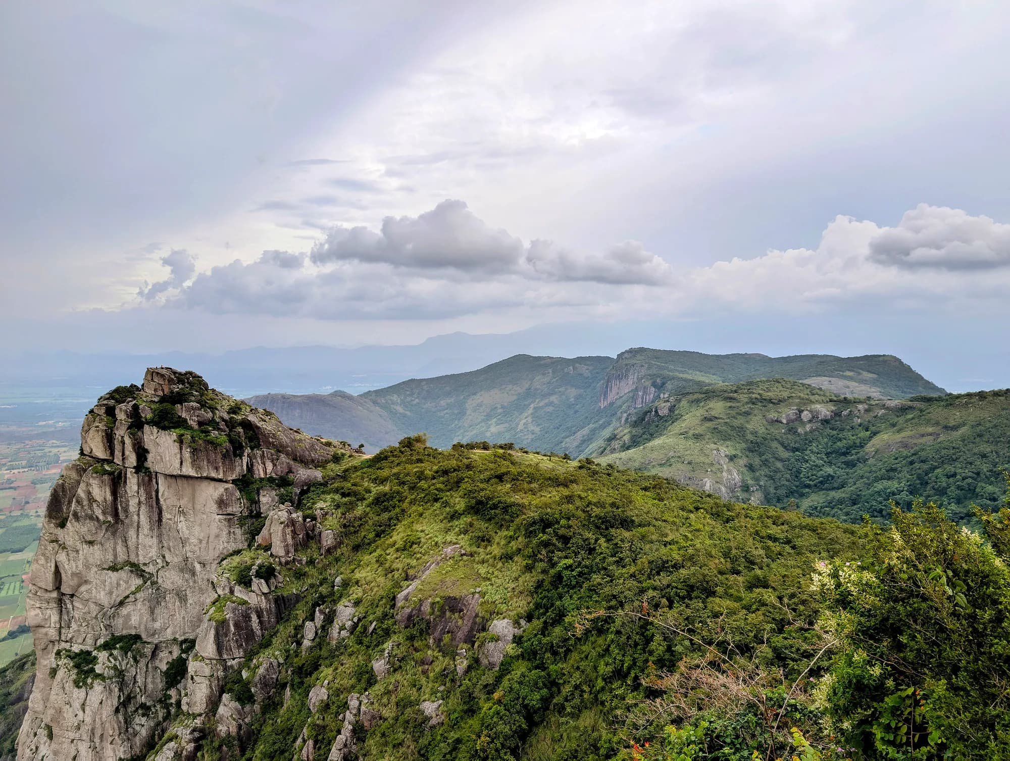 A rocky peak rising above forested hills under a cloudy sky